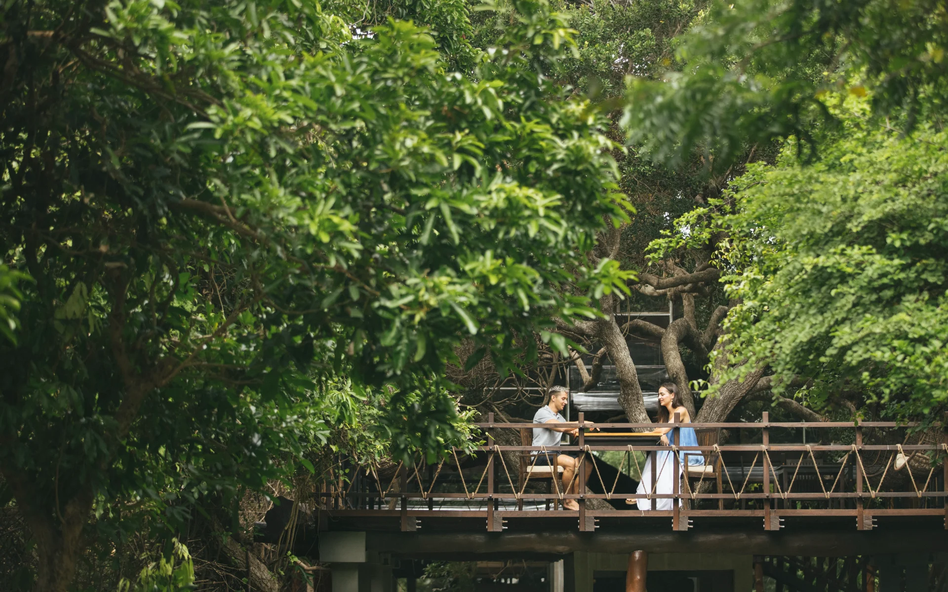 A couple enjoy a signature dining experience on a stilted platform, surrounded by foliage.